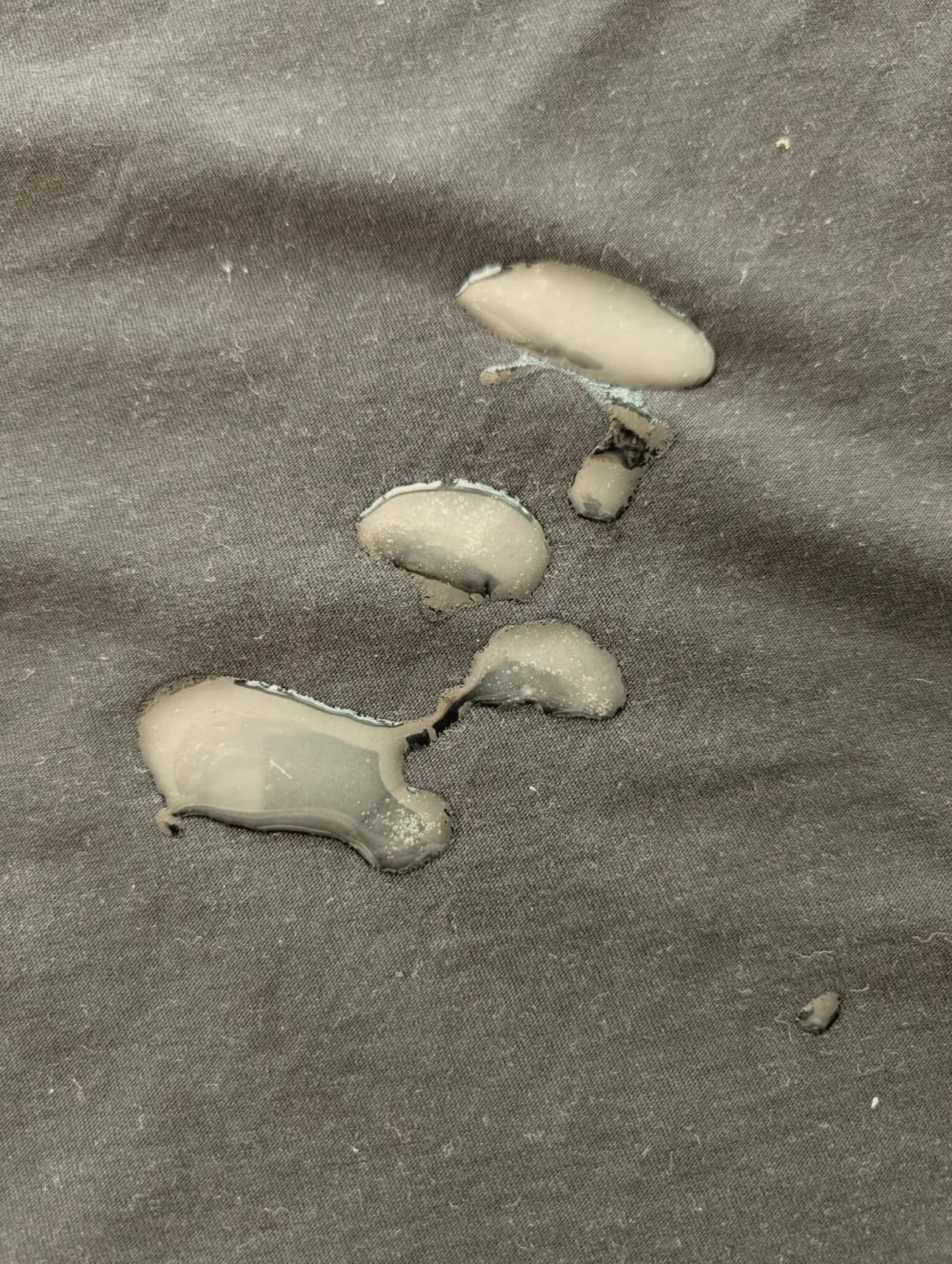 Blobs of creamy white SPUNK Hybrid lube sitting wet and beaded on a black cotton t-shirt, six hours after it was applied