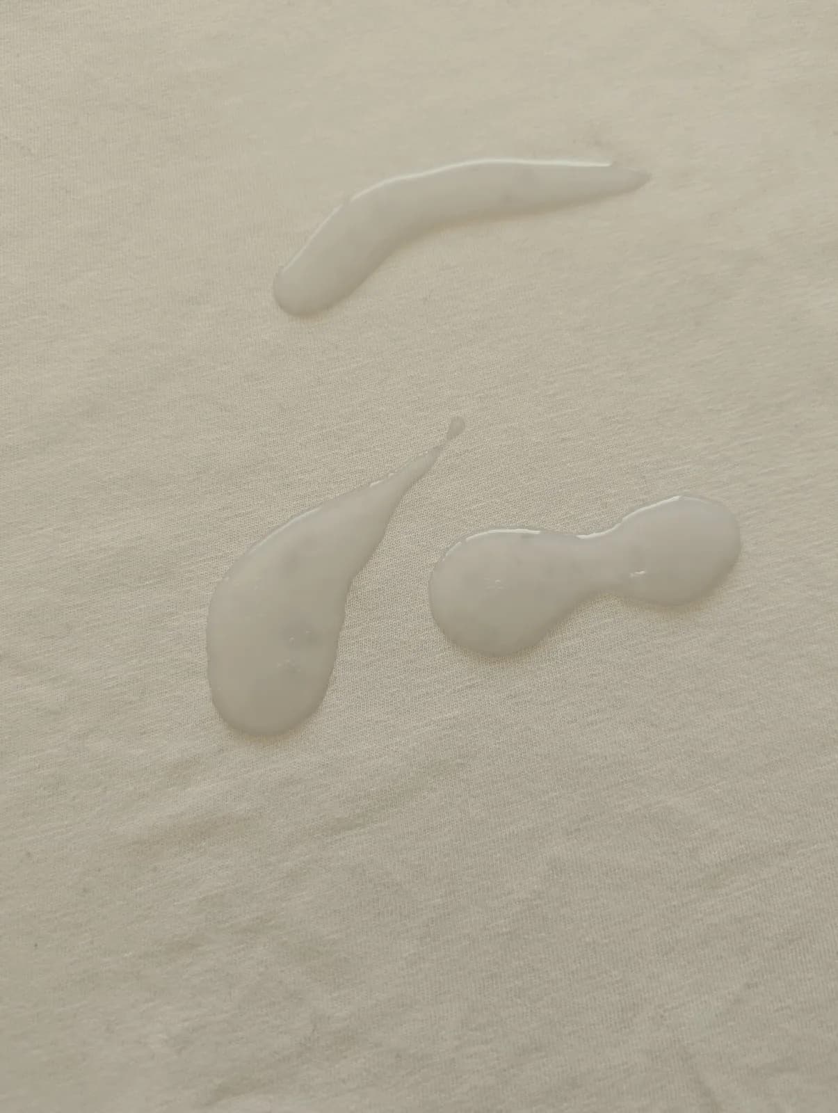Three milky white blobs of SPUNK Hybrid lube still sitting on the surface of a white cotton t-shirt after 6 hours